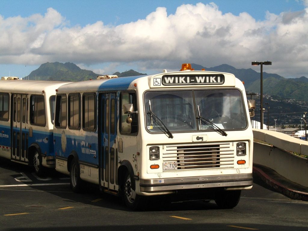 Airports Expand Electric Shuttle Bus Services Passengers board an airport shuttle bus outside a busy modern terminal.